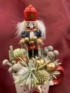 Kép 2/3 - Diótörő Demeter brunniával ékített karácsonyi töltött bögrécskéje tartós virágdísz